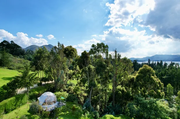 KingDome desde el aire en 2022: un domo entre los árboles, los prados y, al fondo, el Embalse del Tominé y las montañas